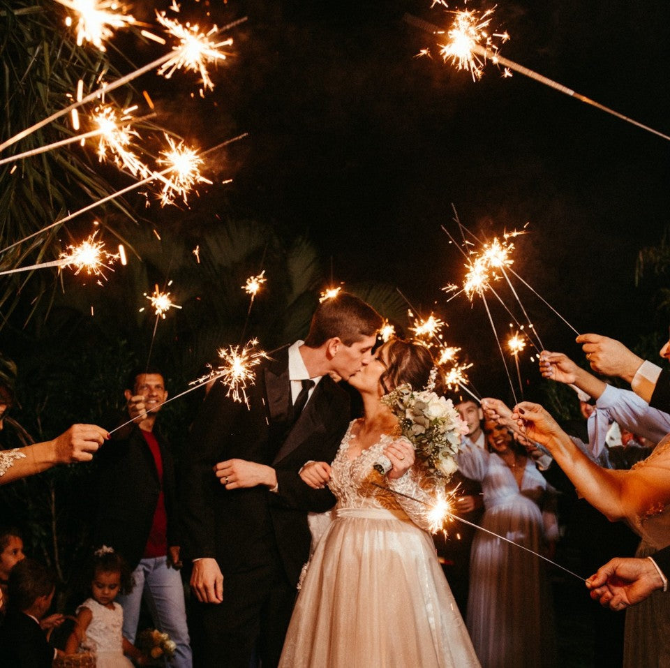 bride and groom kissing while guest hold wedding sparklers